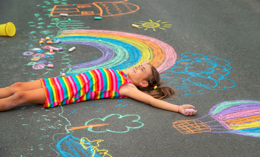 bien-etre-emotionnel Petite fille allongé dans la cour de récréation avec des dessins à la craie par terre
